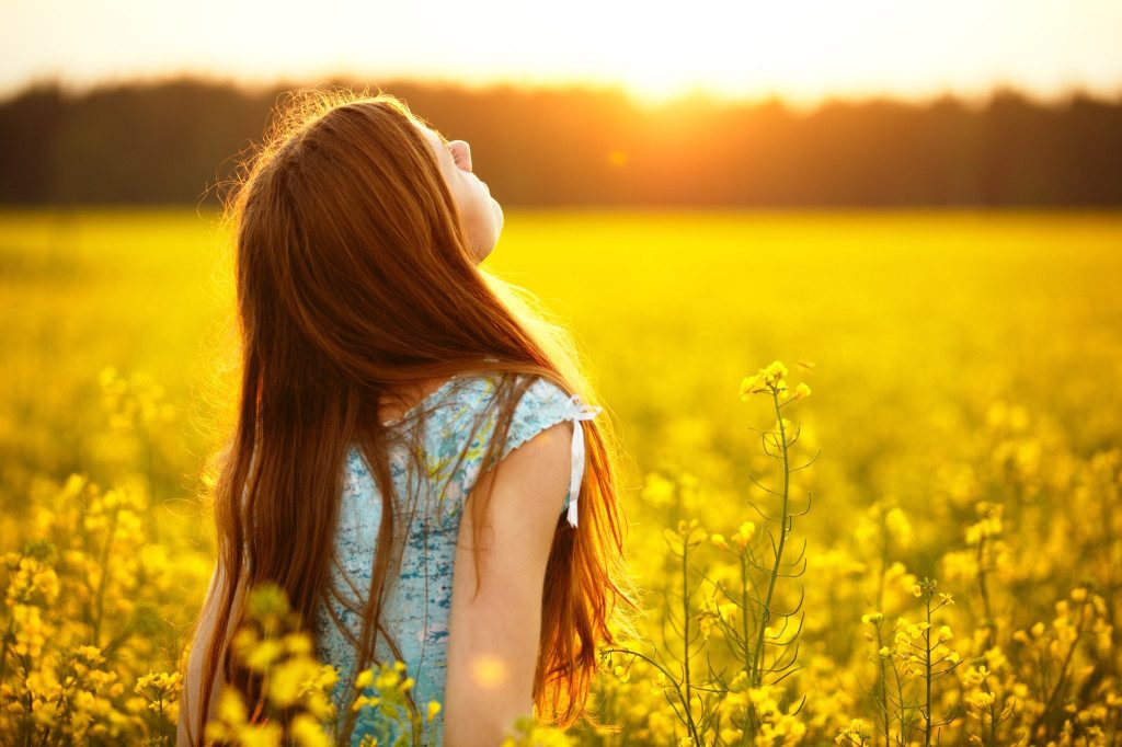 Young woman enjoying nature and sunlight in canola field